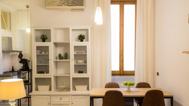 Een moderne keuken met witte kasten, een eettafel met vier stoelen en een raam met gordijnen.