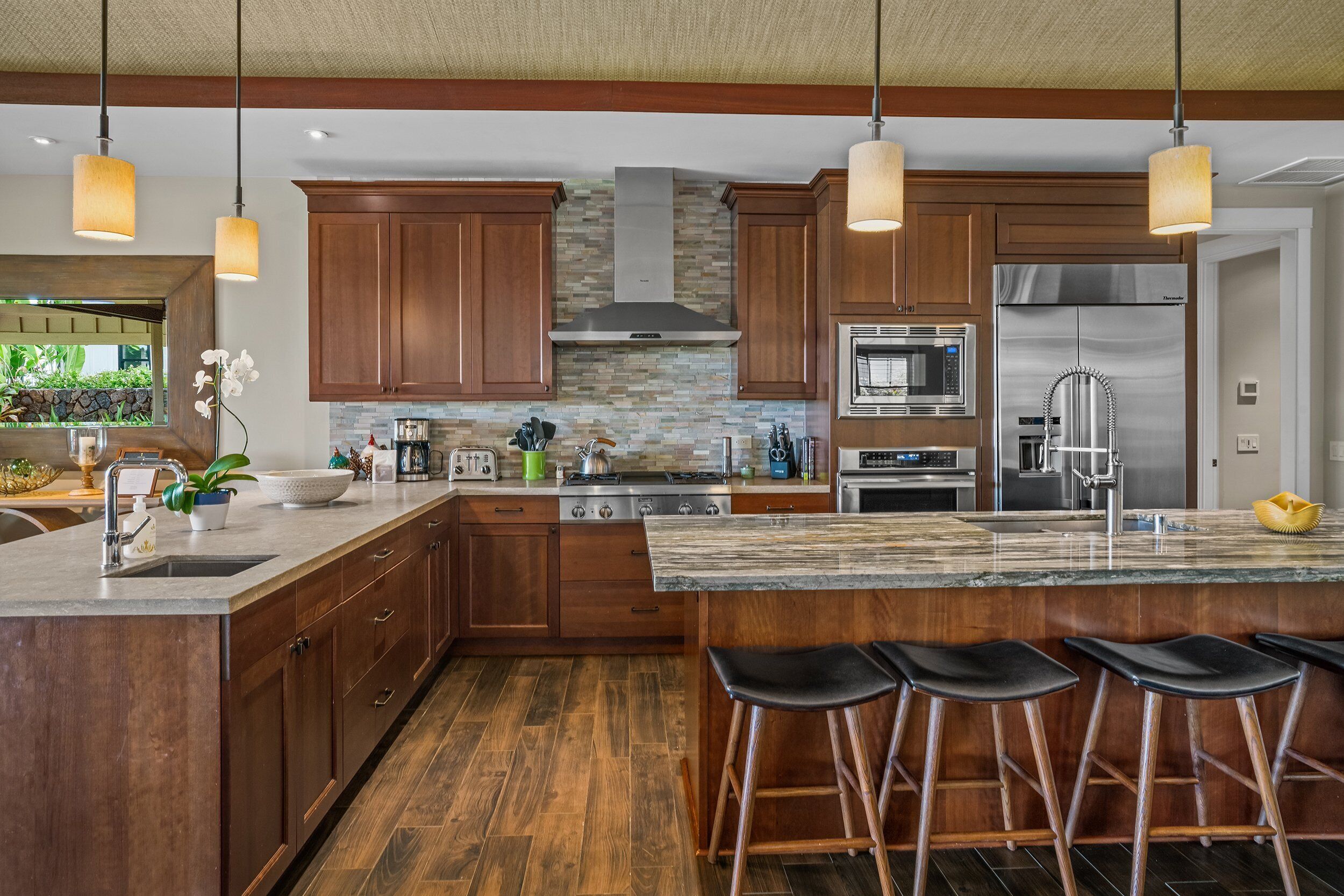 A modern kitchen with wooden cabinets, a large island with bar stools, stainless steel appliances, and pendant lighting.