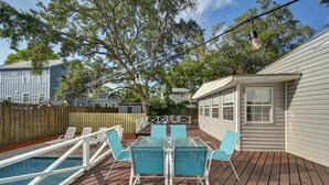 A wooden deck with a glass-top table and chairs, surrounded by a wooden fence and trees.