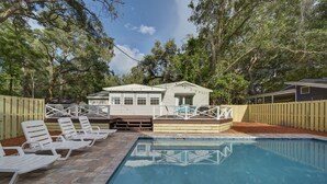 A swimming pool with lounge chairs and a deck, surrounded by a wooden fence and trees.