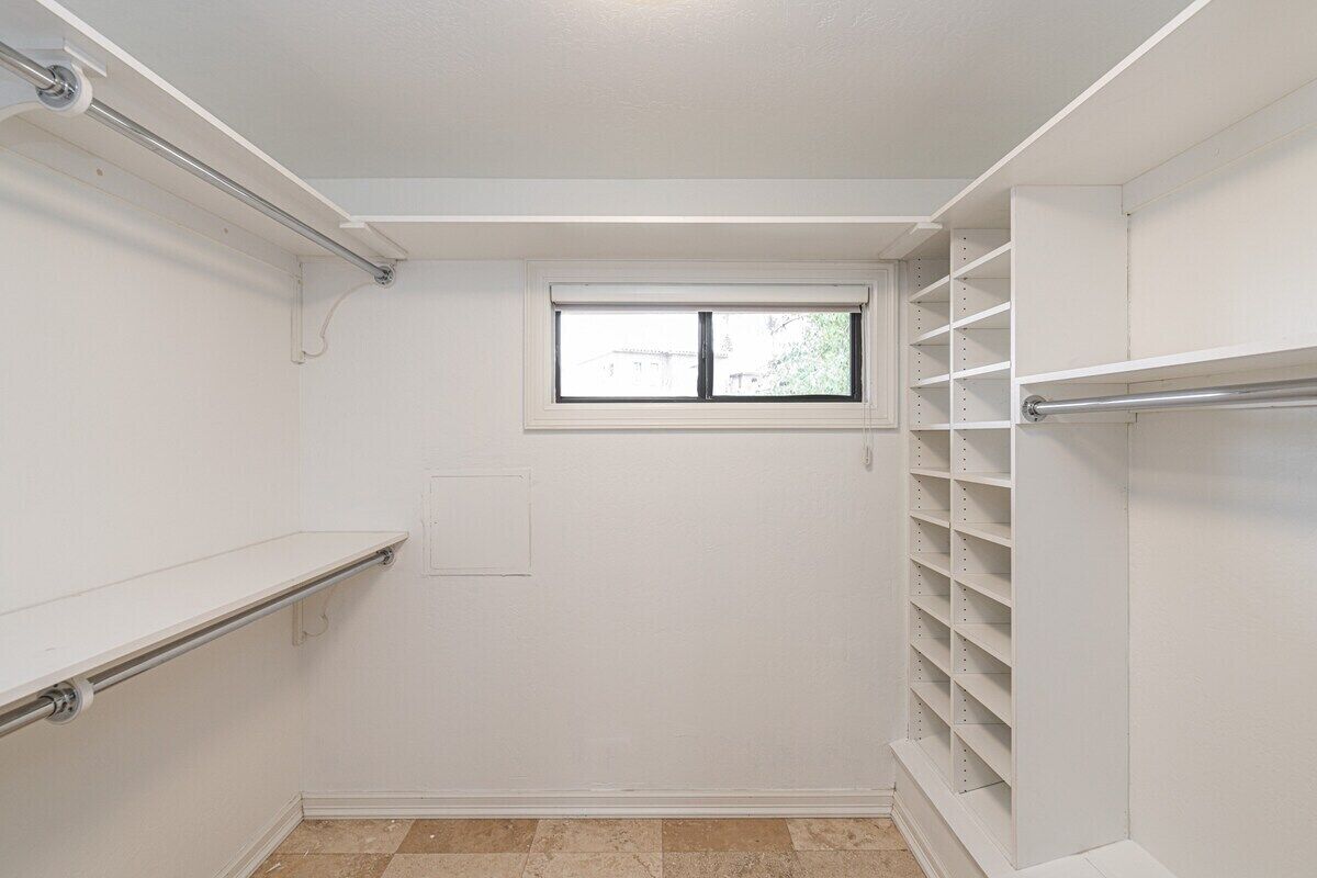 A walk-in closet with a window, shelving, and a door.