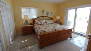 A bedroom with a wooden bed, two nightstands, a ceiling fan, a window with blinds, and a view of the outside. - By The Sea ~ Islamorada Home with Ocean Views! (Islamorada)