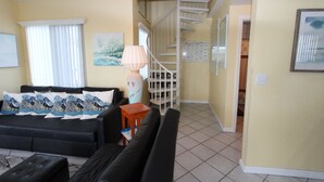 A living room with a black sofa, a wooden side table, and a lamp. There is a staircase leading to another level. - By The Sea ~ Islamorada Home with Ocean Views! (Islamorada)