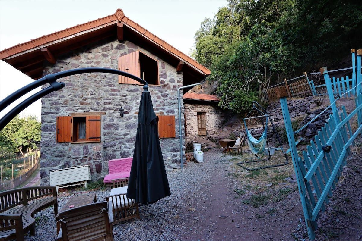 Ein Steinhaus mit Holztür und Fensterläden, einer Hängematte und Sitzgelegenheiten im Freien.