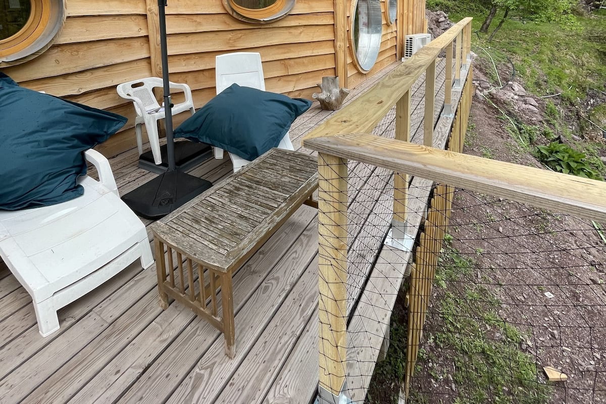 Eine Holzterrasse mit Gartenmöbeln, einem großen Sonnenschirm und einer Holzhütte mit Rundfenstern.