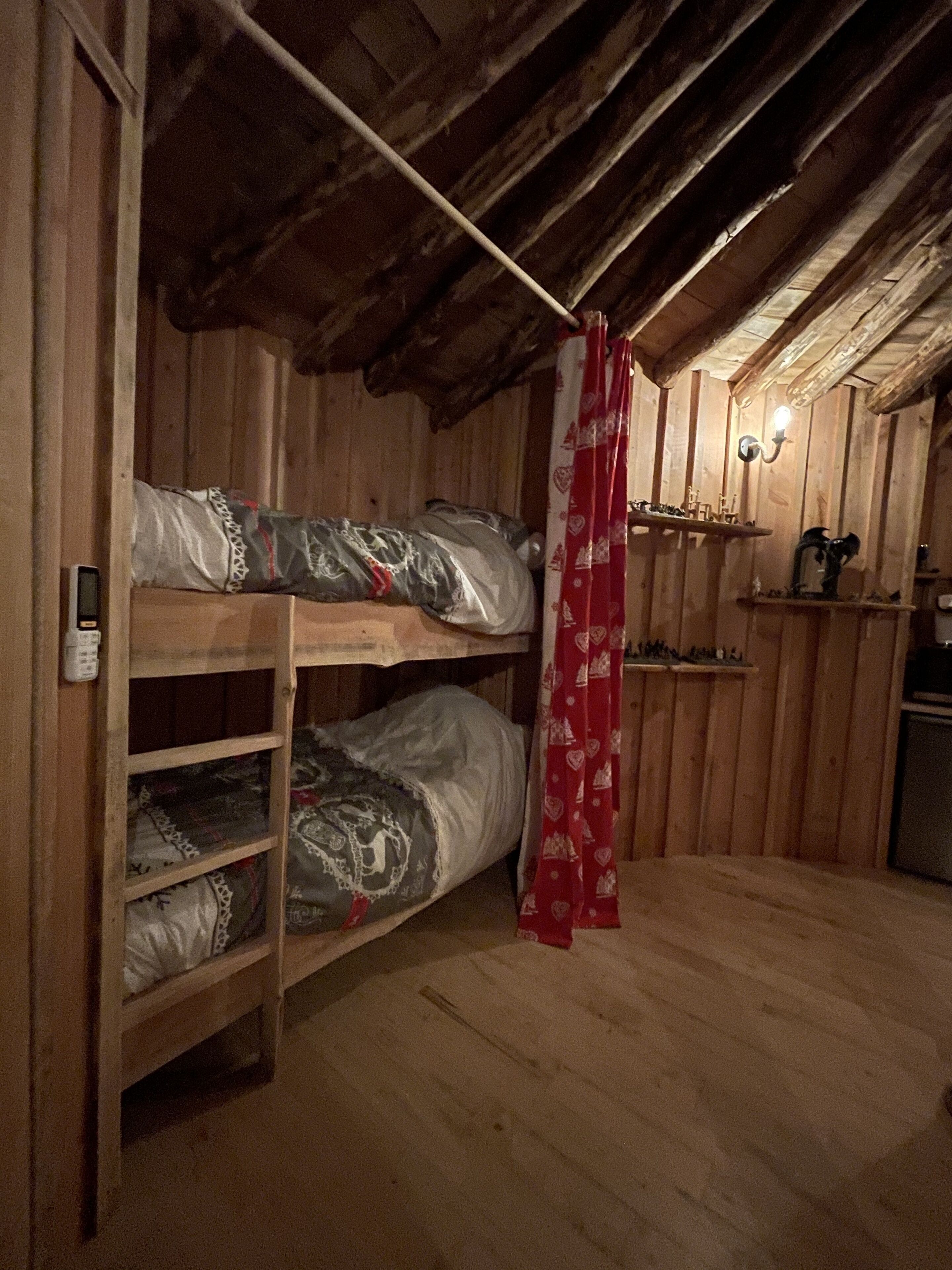 A small, wooden room with bunk beds and a shelf with various items.