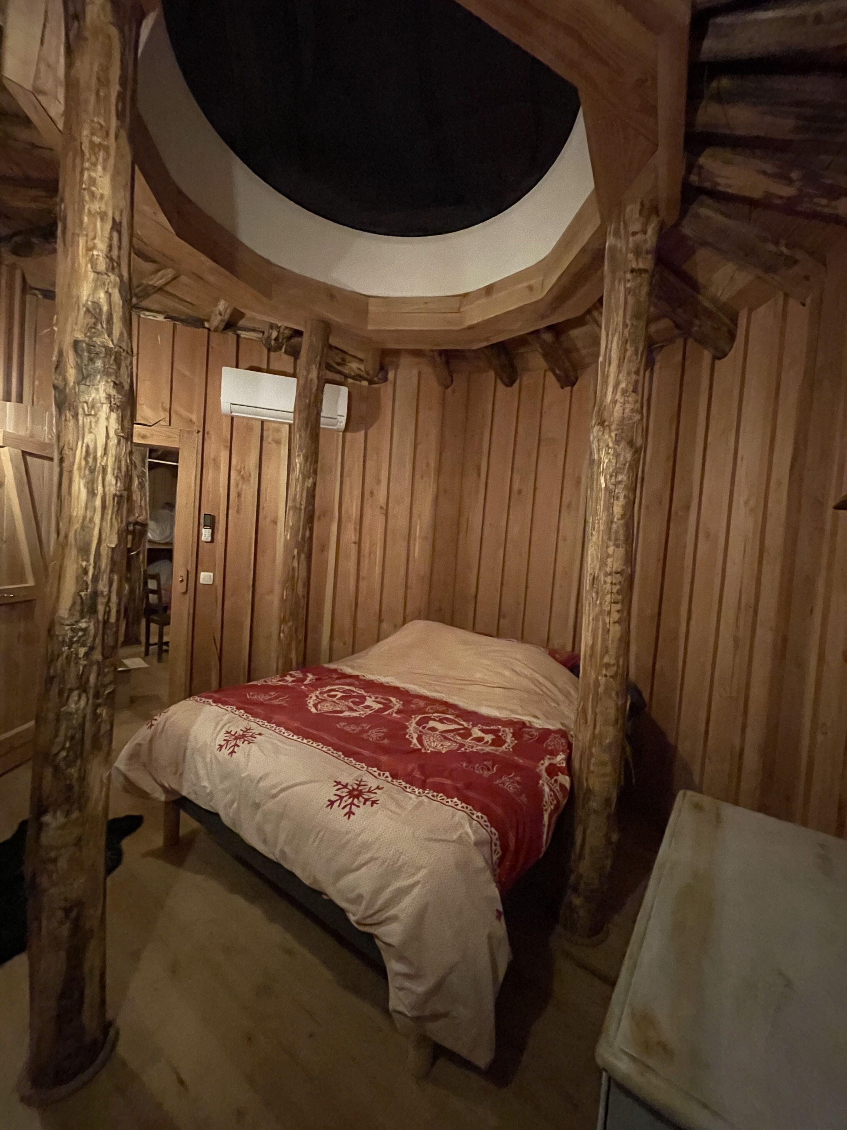 Habitació de fusta amb un llit, una làmpada al sostre i una porta de fusta.