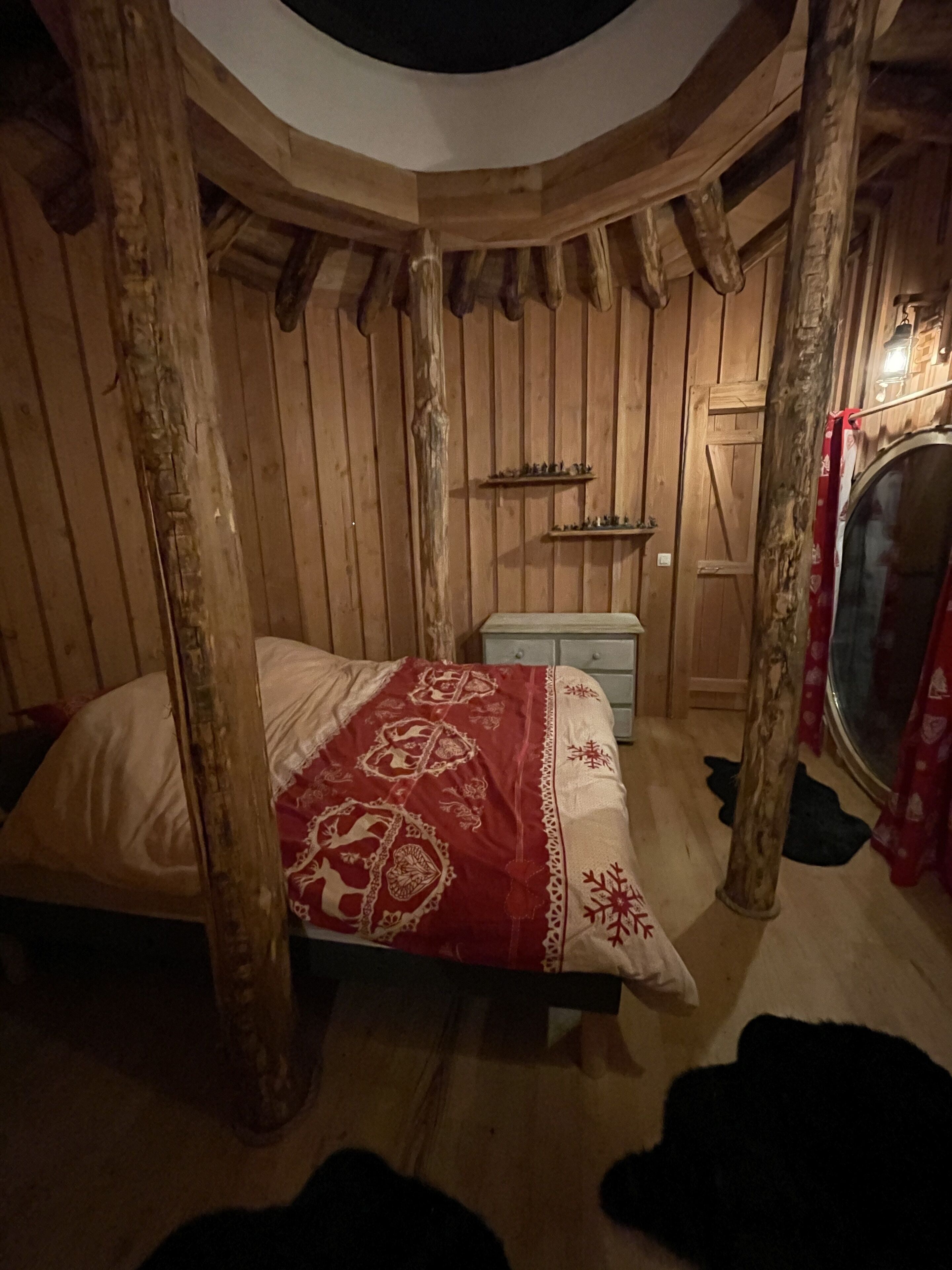 A circular room with wooden walls and a bed with a red and white patterned bedspread.