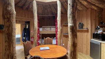 Een houten interieur met een ronde tafel en stoelen, een keukenhoek en een uitzicht door een rond dakvenster.