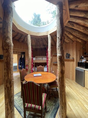 A wooden interior with a round table and chairs, a kitchen area, and a view through a circular skylight. - Les Ecrins de Belvedere (Belvedere)