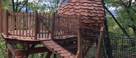 A wooden observation tower with a netted walkway leading to a spherical structure.