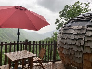 Una terraza de madera con una mesa, sillas, un paraguas rojo y una estructura de techo de paja.