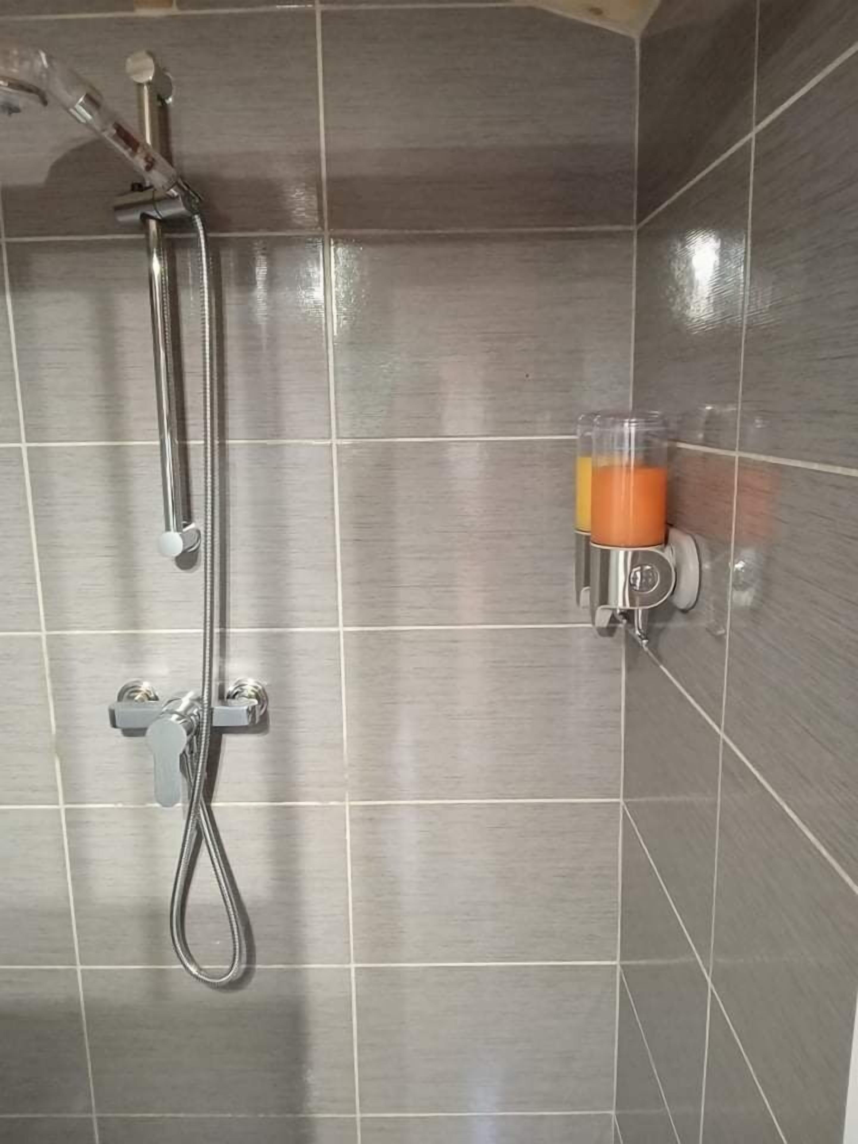 A shower area with a handheld showerhead and a glass container with a yellow liquid, possibly a cleaning product.