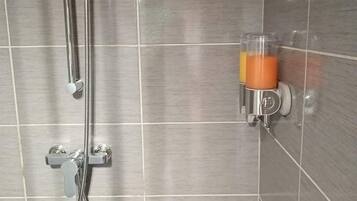 A shower area with a handheld showerhead and a glass container with a yellow liquid, possibly a cleaning product.