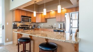 A kitchen with wooden cabinets, a granite countertop, stainless steel appliances, and pendant lighting. - Sleek & Stylish- Riverside (Pensacola)