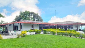 Un edificio con techo rojo, paredes blancas y un patio cubierto con mobiliario exterior.