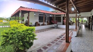 Un espacio al aire libre cubierto con suelo de baldosas, un edificio con techo rojo y un jardín con plantas amarillas y verdes.