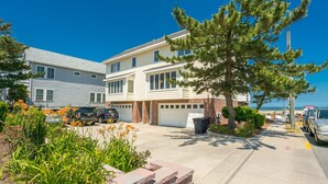 A two-story residential building with a garage, a driveway, and a parking area with cars.