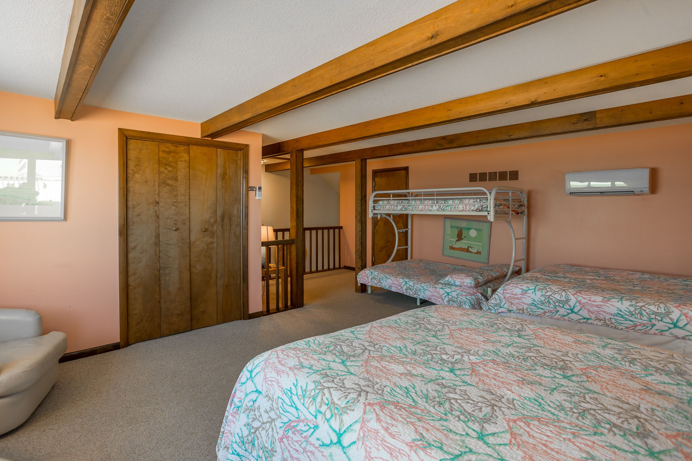 A bedroom with two bunk beds, a wooden ceiling, a door, and an air conditioning unit.