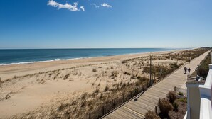 A beach view with a wooden boardwalk, sandy dunes, and the ocean.