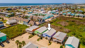 Un quartier résidentiel en bord de mer, avec des maisons aux couleurs vives, une plage en arrière-plan et un ciel dégagé.
