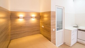 A bedroom with a bed, a small kitchenette, and a bathroom with a glass door. - Smart Apartment Kulisha 29v (Lviv)