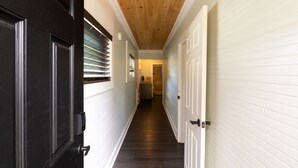 A hallway with a wooden ceiling, white walls, and a dark floor. - Treehouse Suite: Walk DNTN | Lux Apt | Pet Welcome (Gainesville)
