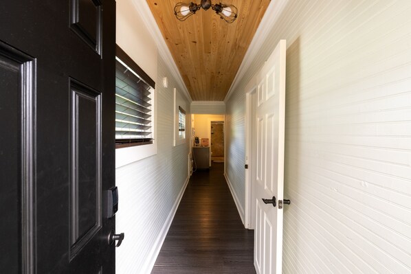 Un couloir avec un plafond en bois, des murs blancs et un plancher foncé.