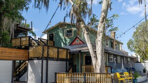A two-story house with a porch, a staircase, and a fenced outdoor seating area. - Treehouse Suite: Walk DNTN | Lux Apt | Pet Welcome (Gainesville)