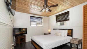 A bedroom with a bed, a TV, a ceiling fan, wooden flooring, and a window with blinds. - Treehouse Suite: Walk DNTN | Lux Apt | Pet Welcome (Gainesville)