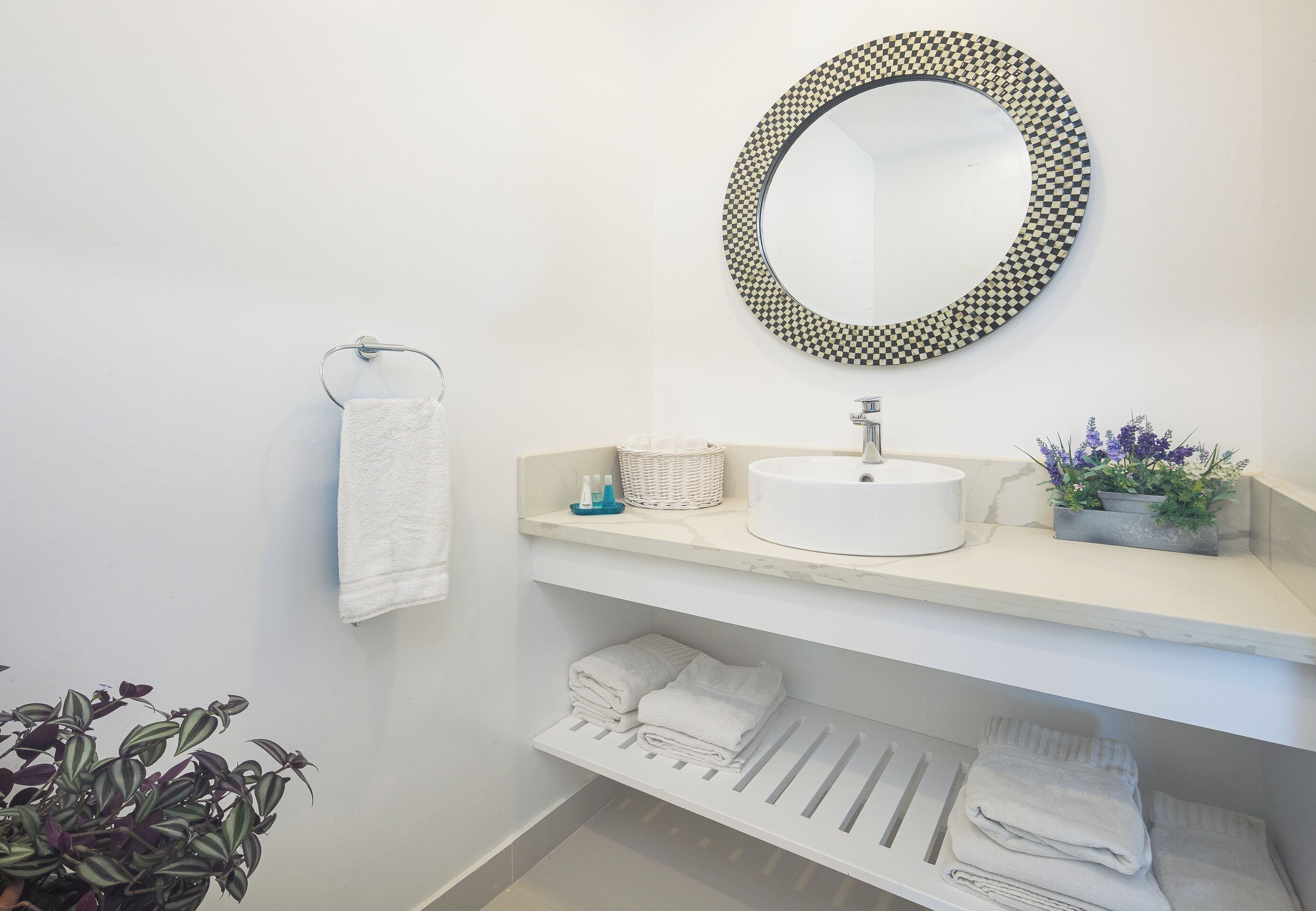 A bathroom with a round mirror, a sink, a towel rack, and a shelf with folded towels.