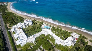 Vue aérienne d’un hôtel situé sur la côte, composé de plusieurs bâtiments, avec une piscine et une plage.