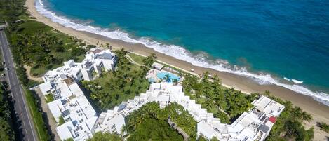 An aerial view of a coastal hotel with multiple buildings, a swimming pool, and a beach.