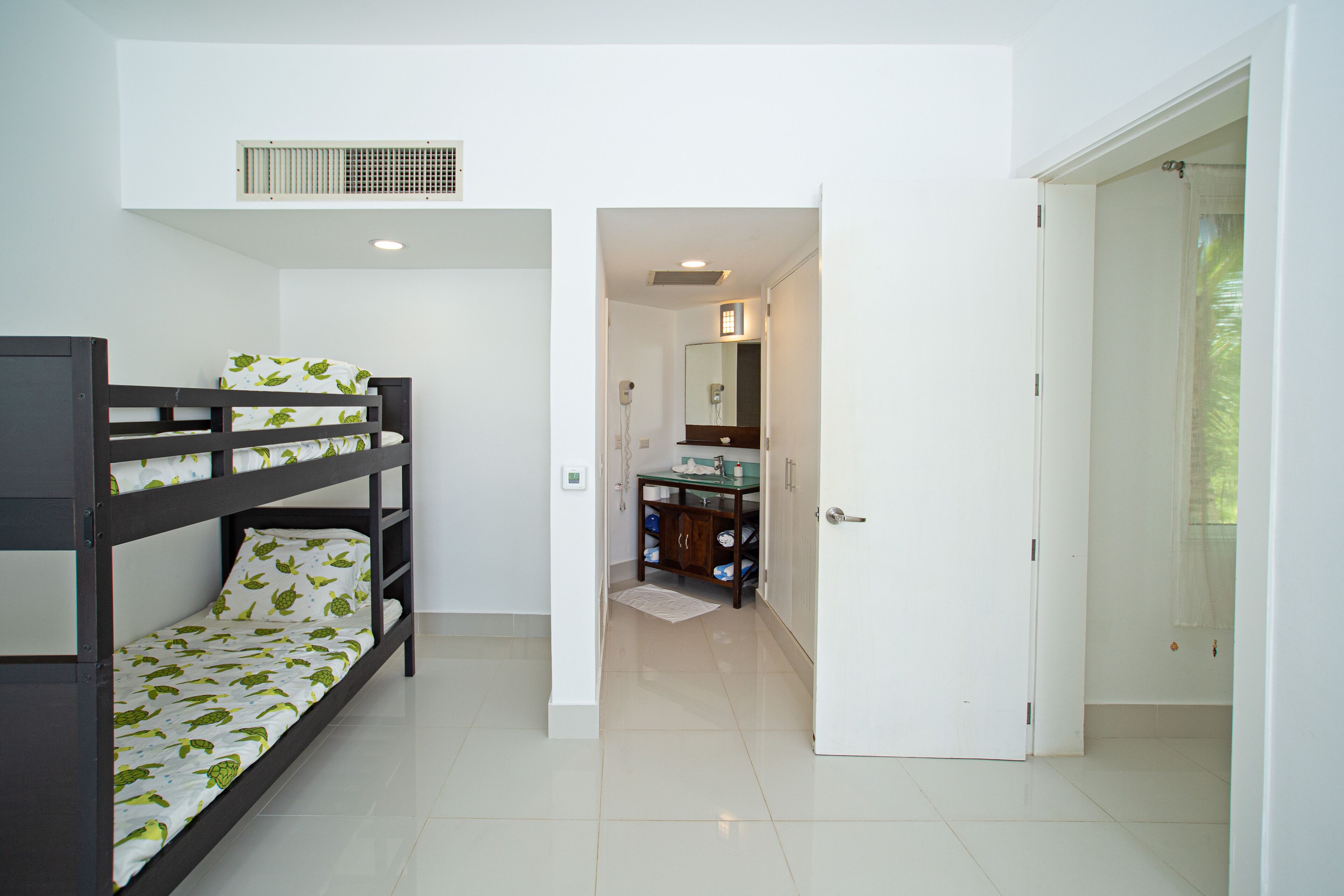 A room with bunk beds, a bathroom with a mirror, and a door leading to another room.