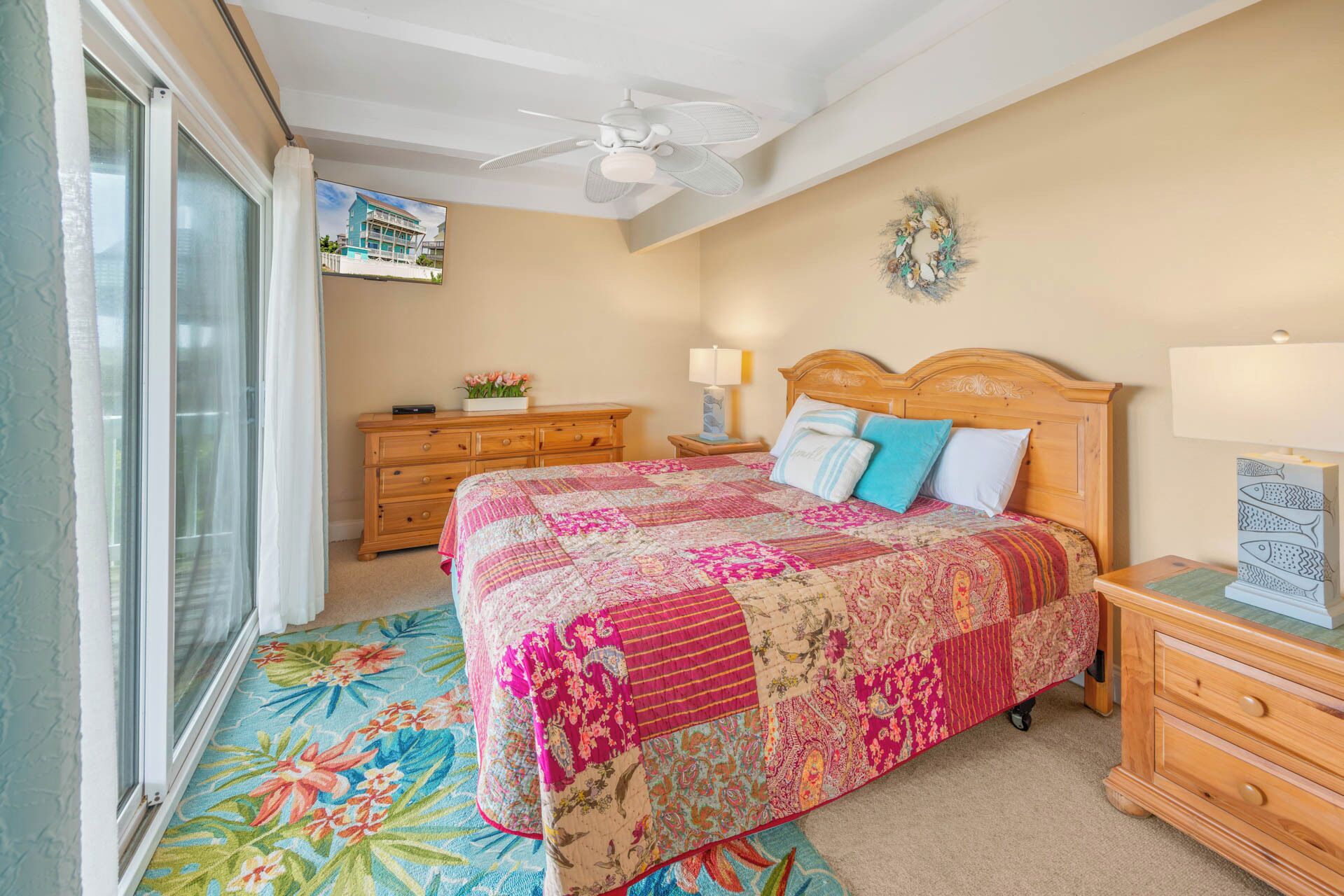 Une chambre à coucher avec un grand lit, une commode en bois, une table de chevet, un ventilateur de plafond et une fenêtre avec des rideaux.