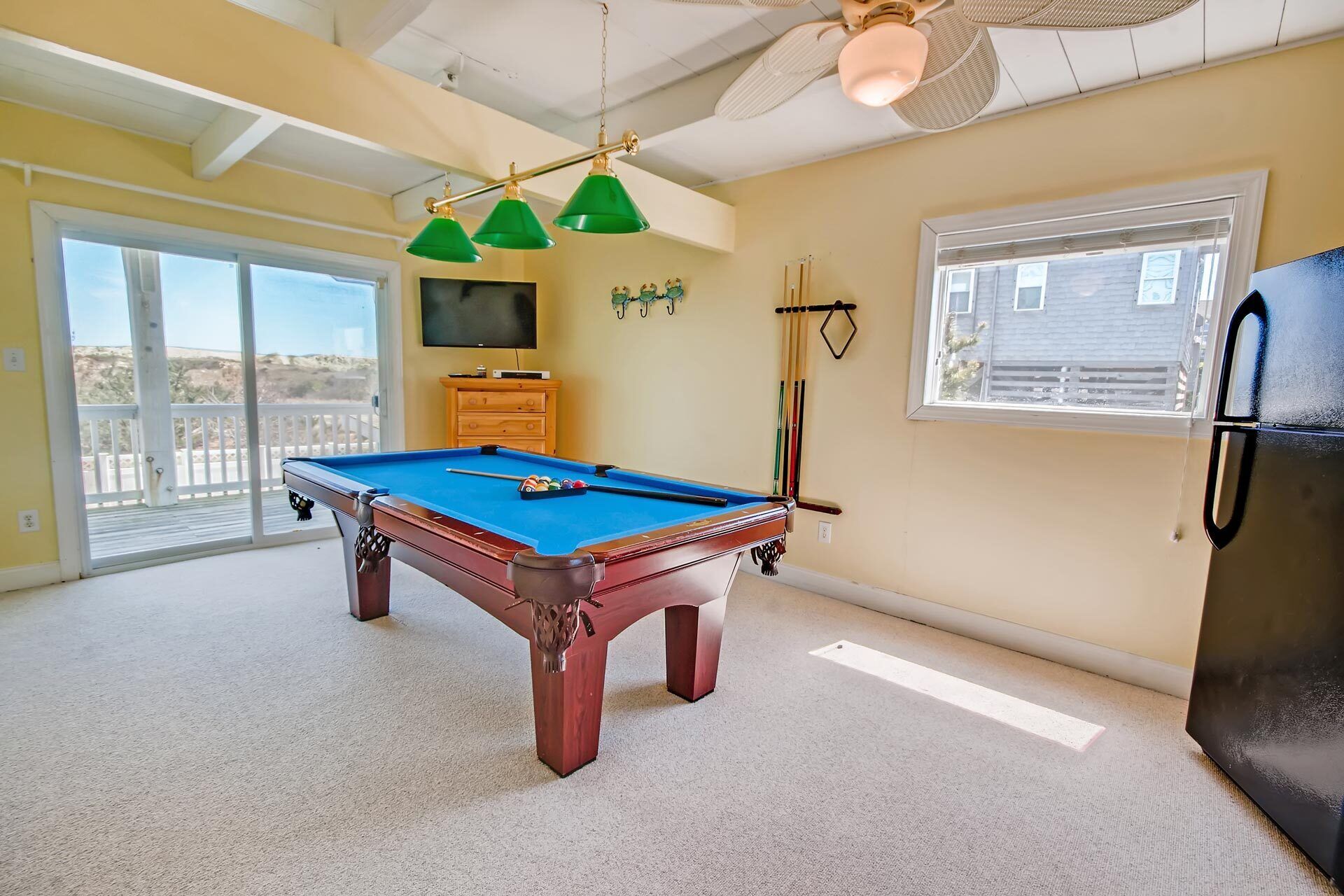 A pool table in a room with a ceiling fan, a television, and a window with blinds.