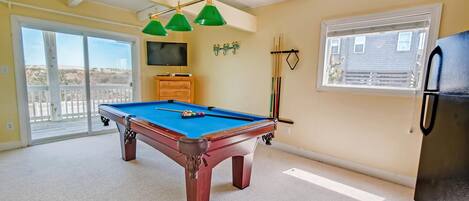 A pool table in a room with a ceiling fan, a television, and a window with blinds.