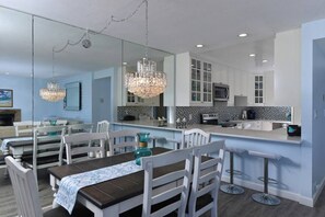 A modern kitchen with white cabinets, a central island, and a dining area with a wooden table and white chairs. - Bay Condo · Clean Bay Front 2bedroom 2bath Condo with Garage (San Diego)