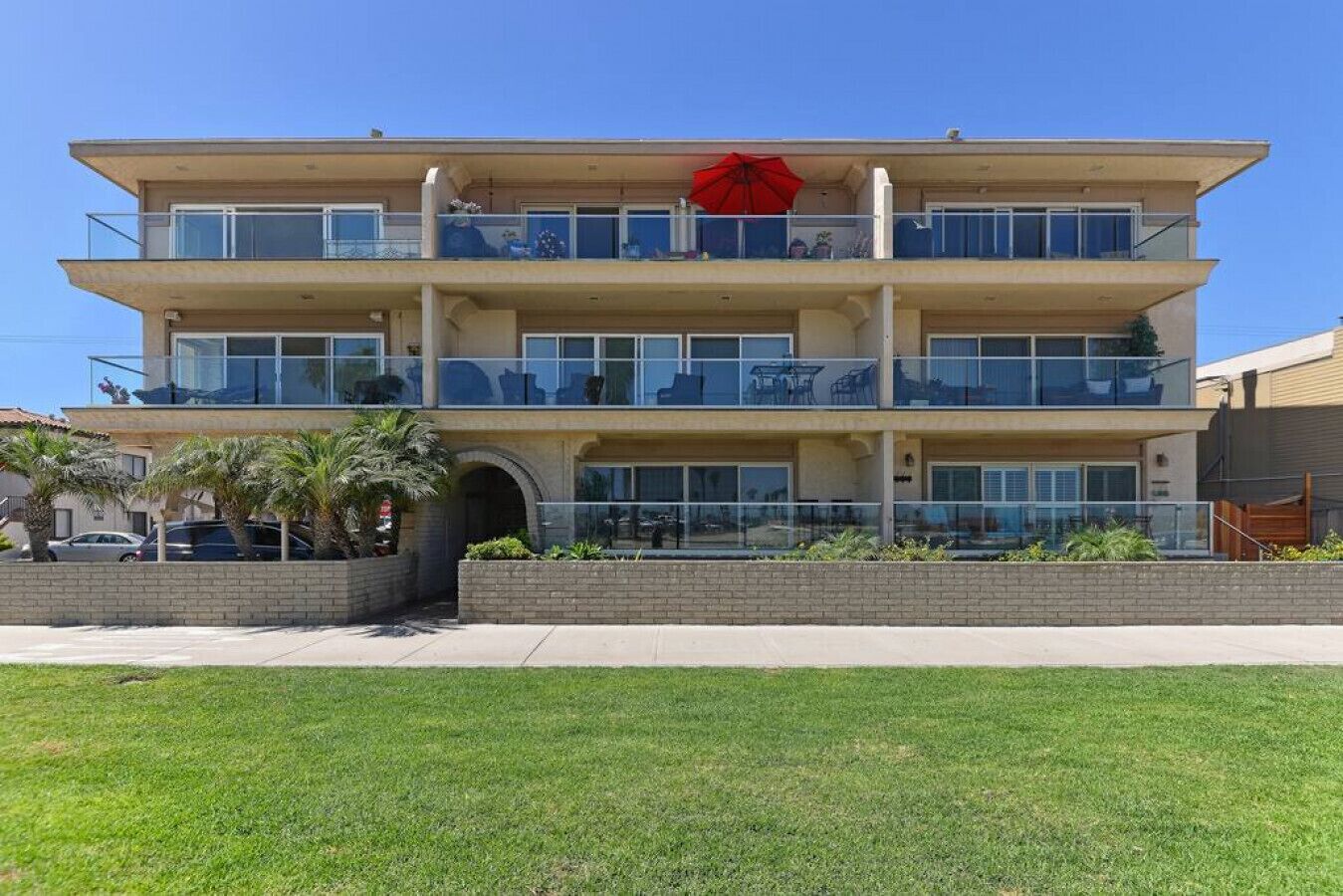 A multi-story building with balconies, a red umbrella, and a clear sky.