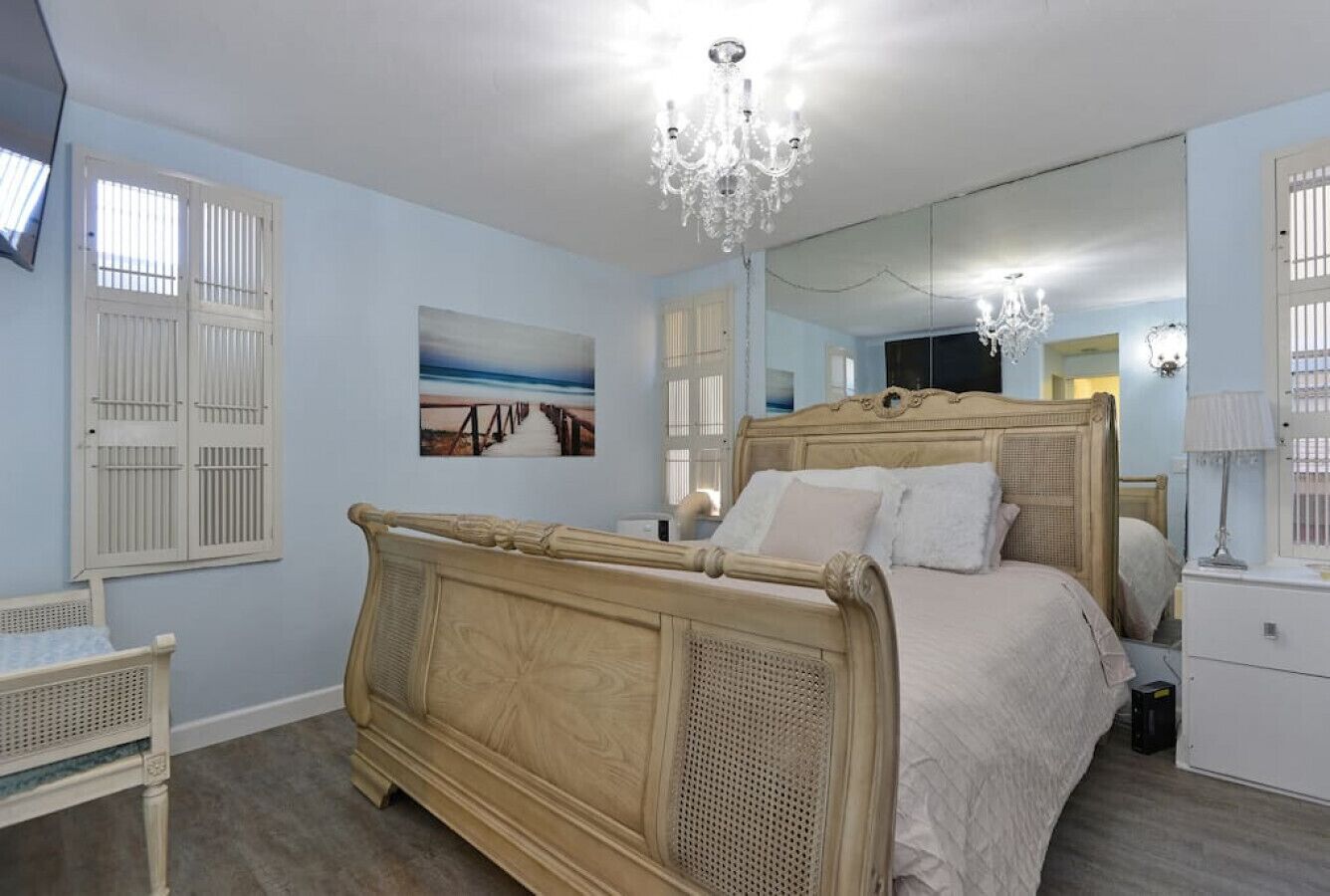 A bedroom with a large bed, a bedside table, a mirror, and a chandelier.