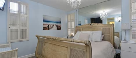 A bedroom with a large bed, a bedside table, a mirror, and a chandelier.