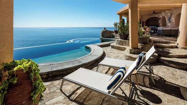Un área junto a la piscina con sillones de descanso, una piscina de piedra y vista al océano.