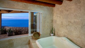 Un baño con una bañera grande, vista al océano a través de un ventanal corredero y plantas en macetas.