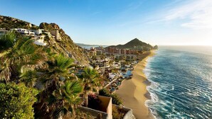 Un complejo turístico frente al mar, con palmeras y montañas al fondo.