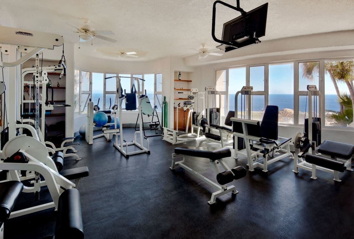 A gym with various exercise equipment, large windows, and a view of the ocean.