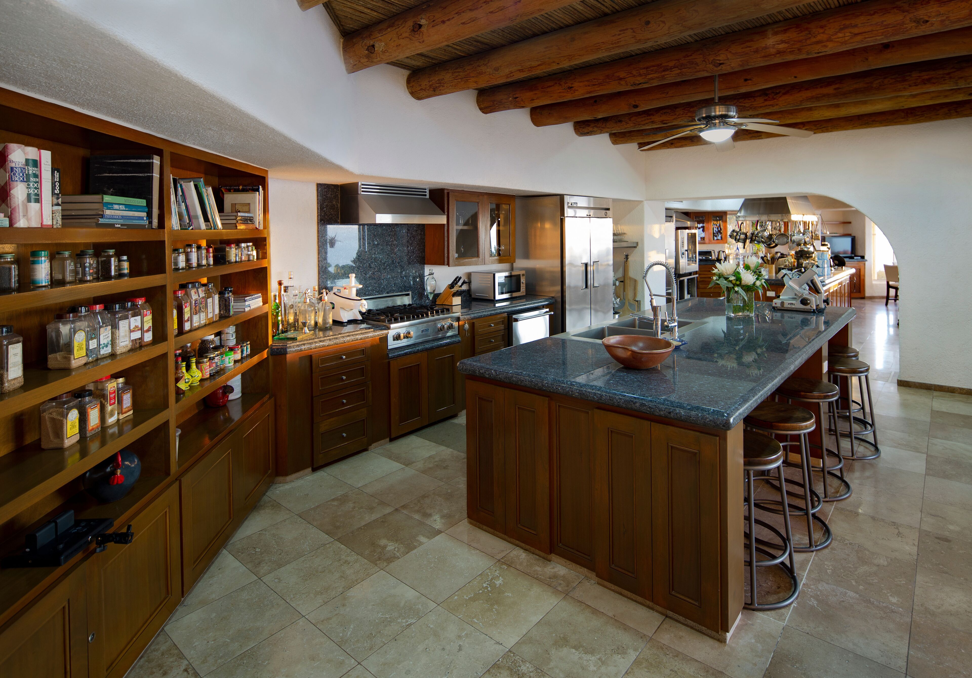 Una cocina amplia con armarios de madera, una isla central con taburetes, microondas, estufa y refrigerador.