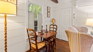 A dining area with a wooden table and chairs, a lamp, and framed pictures on the wall. - Quaint Guest Cottage 1 block from Beach updated July 2022 (Saint Simons Island)
