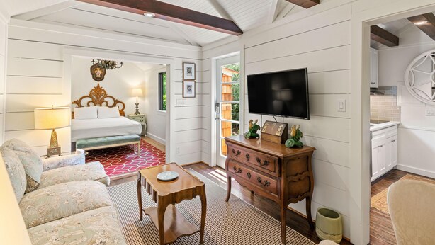 A cozy room with a bed, a TV, a wooden dresser, and a dining area. - Quaint Guest Cottage 1 block from Beach updated July 2022 (Saint Simons Island)