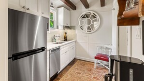 A modern kitchen with white cabinets, a stainless steel refrigerator, a dishwasher, and a red chair. - Quaint Guest Cottage 1 block from Beach updated July 2022 (Saint Simons Island)