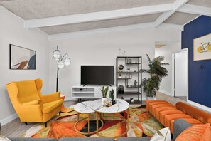 A modern living room with a sofa, armchair, TV, and decorative plants. - Vibrant House w Great Backyard, Pool and Jacuzzi (Irving)